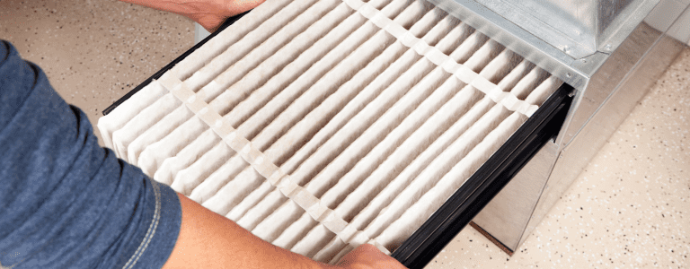 An outdoor air conditioning unit installed next to a brick house, surrounded by a landscaped garden with plants and mulch