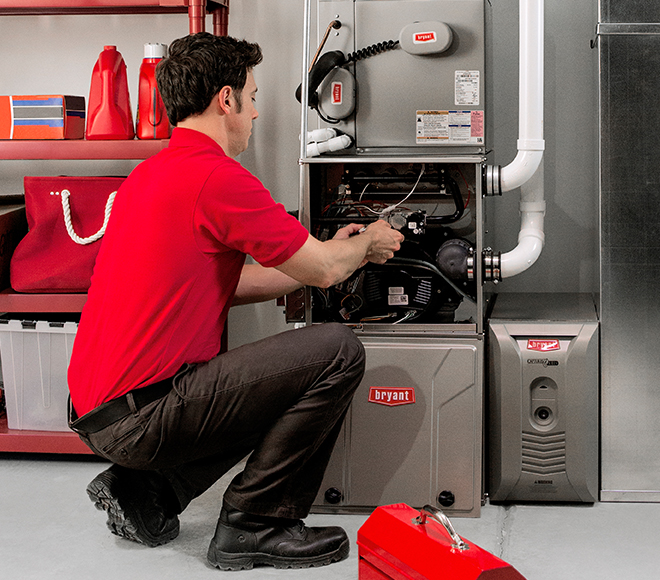 Technician in red shirt repairing a Bryant furnace in a basement
